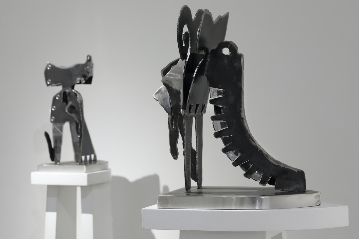 two abstract obsidian sculptures on white podiums in a white gallery space