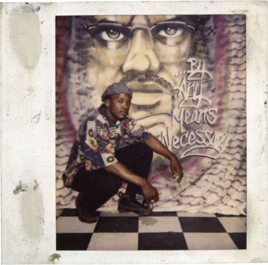 scanned polaroid of black man crouching in front of a graffiti backdrop on a black and white checker floor