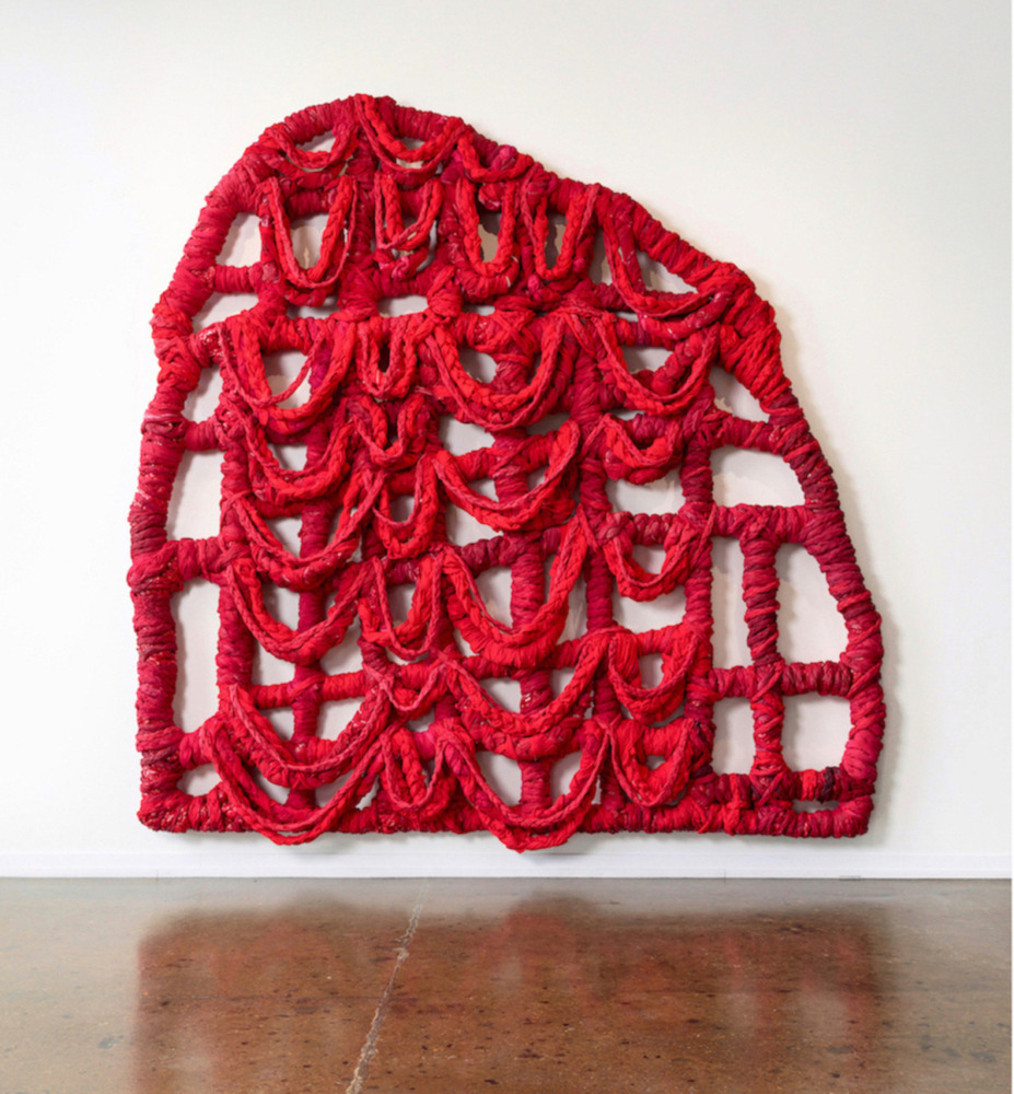 a large red woven textile mounted on to a wall. it is reflected on the ground below it