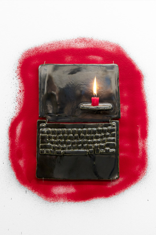 a ceramic model of a laptop on a wall with a short red candle